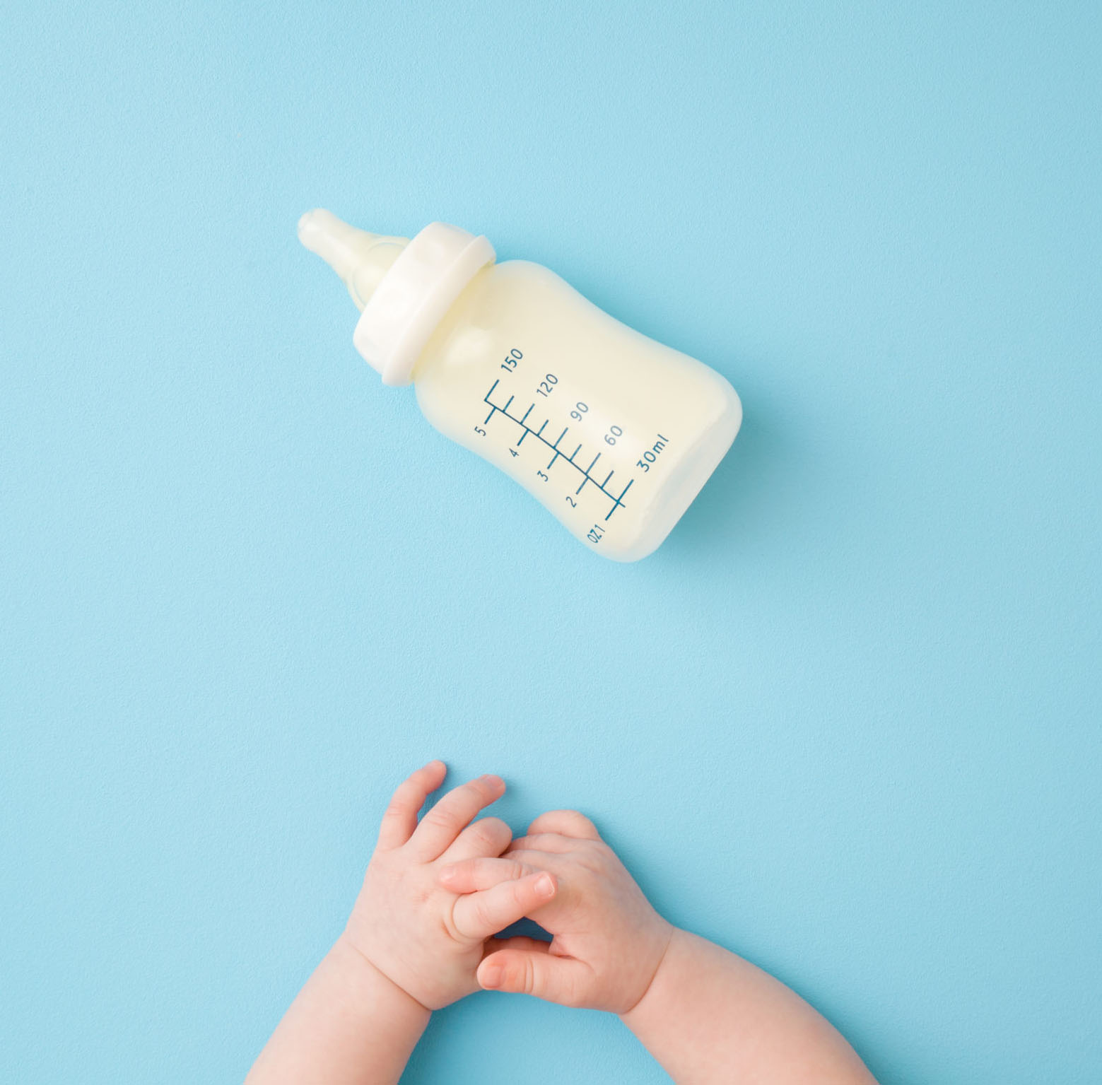 baby's hands clasped on blue background with empty formula bottle