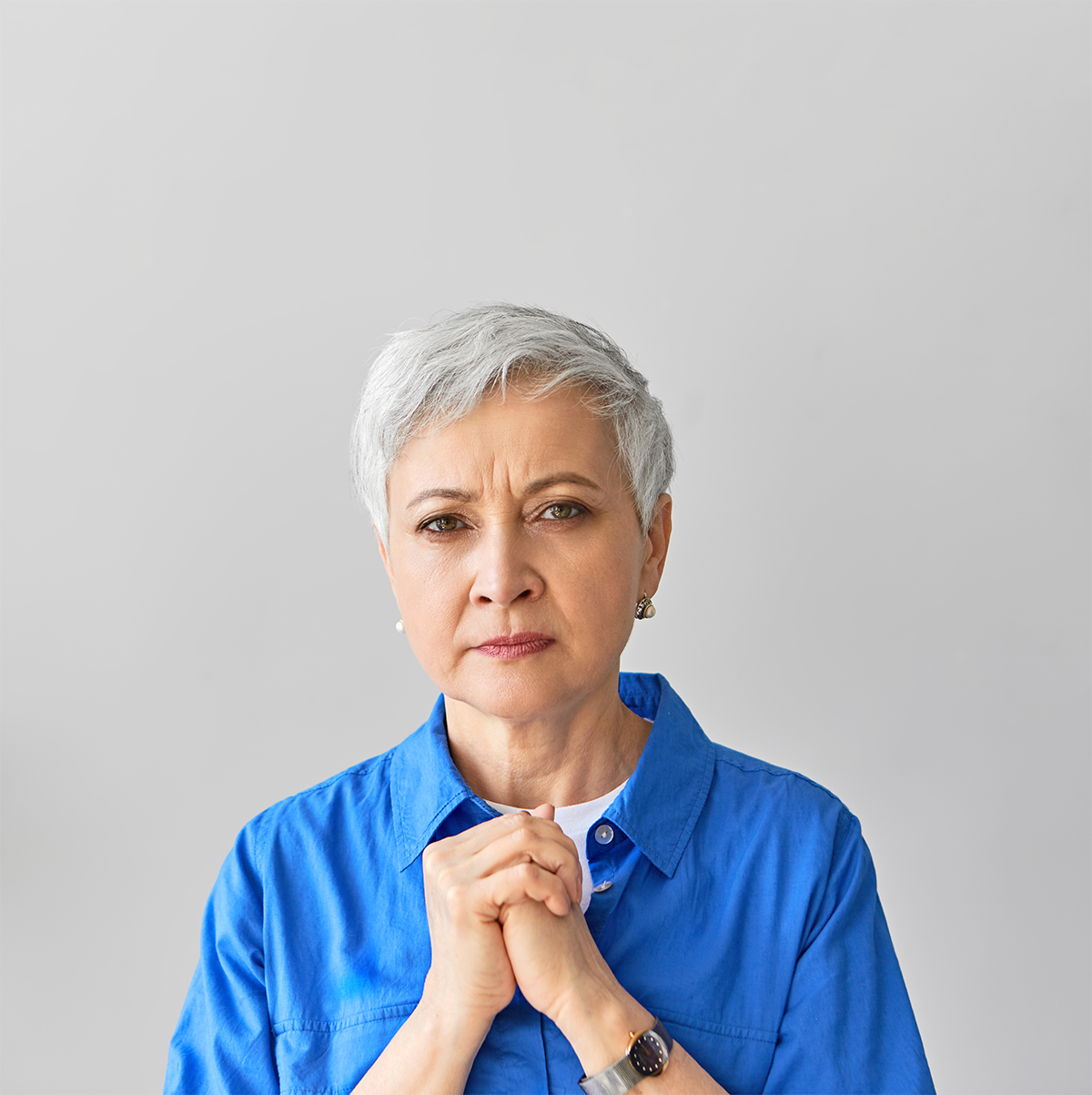 worried mature gray haired female clasping hands to chest